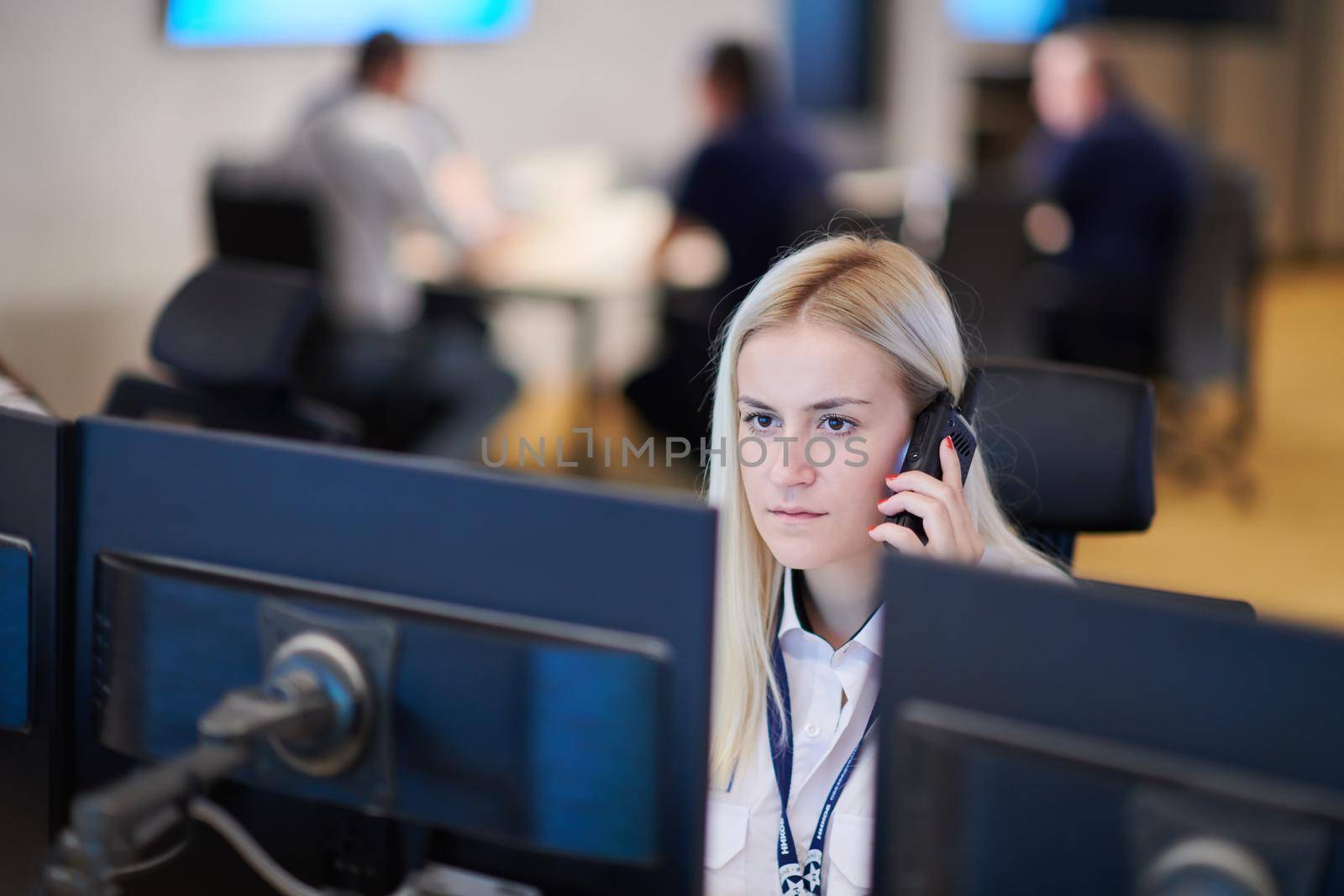 Female security guard operator talking on the phone while working at workstation with multiple displays Security guards working on multiple monitors