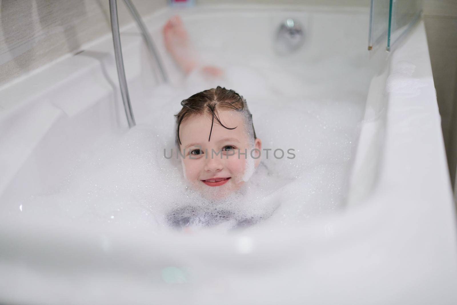 little girl playing with soap foam in bath during coronavirus stay at home pandemic quarantine