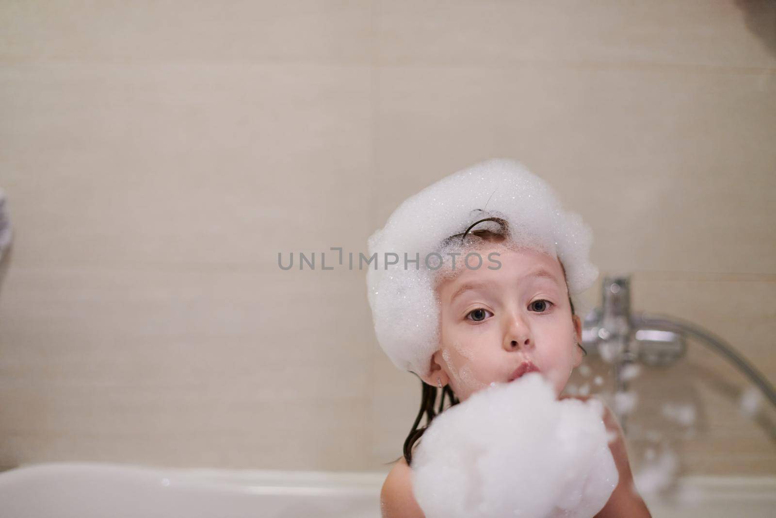 little girl playing with soap foam in bath during coronavirus stay at home pandemic quarantine