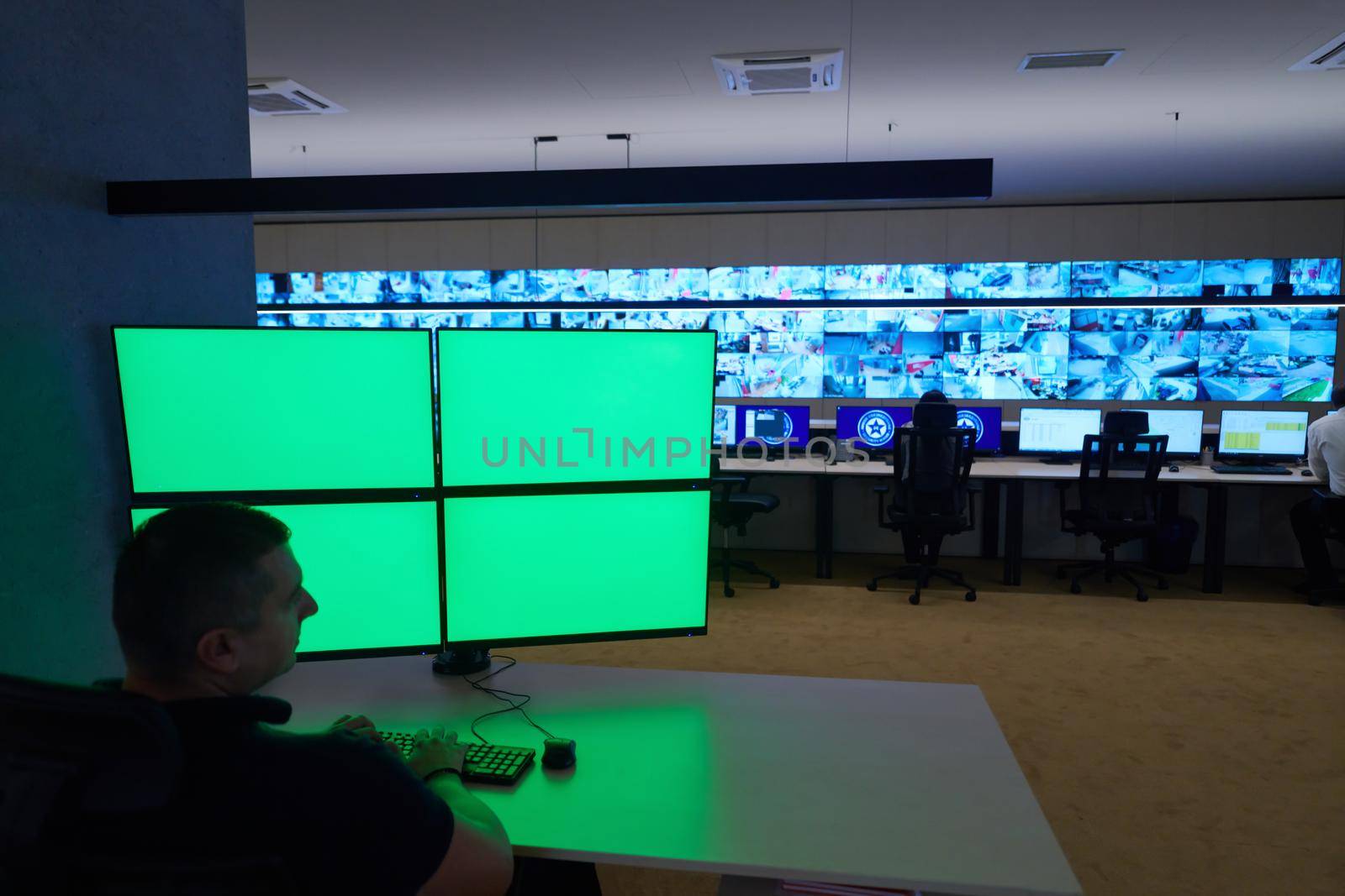 Male security operator working in a data system control room offices Technical Operator Working at  workstation with multiple displays, security guard working on multiple green blank screens  Male computer operator monitoring from a security center