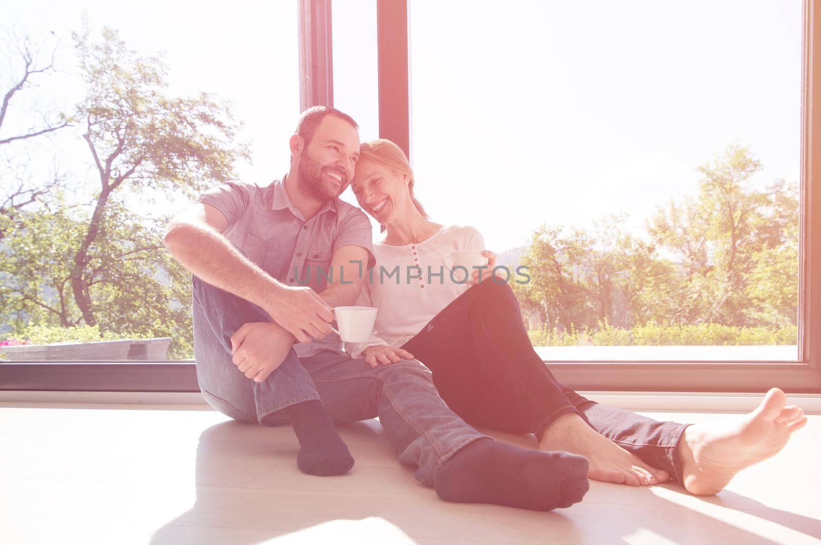 happy romantic couple enjoying morning coffee on the floor by the window in their luxury home
