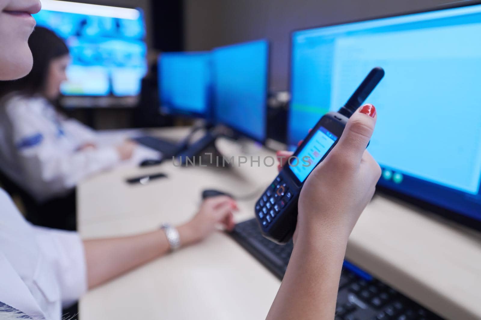 Female security operator holding portable radio in hand while working in a data system control room offices Technical Operator Working at  workstation with multiple displays, security guard working on multiple monitors