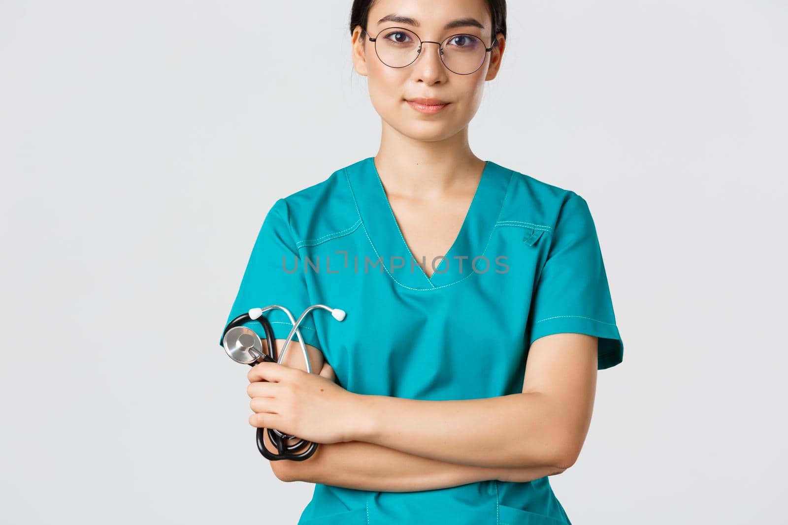 Covid-19, coronavirus disease, healthcare workers concept. Confident smiling professional asian doctor in glasses, cross arms chest, wearing scrubs and holding stethoscope, white background.
