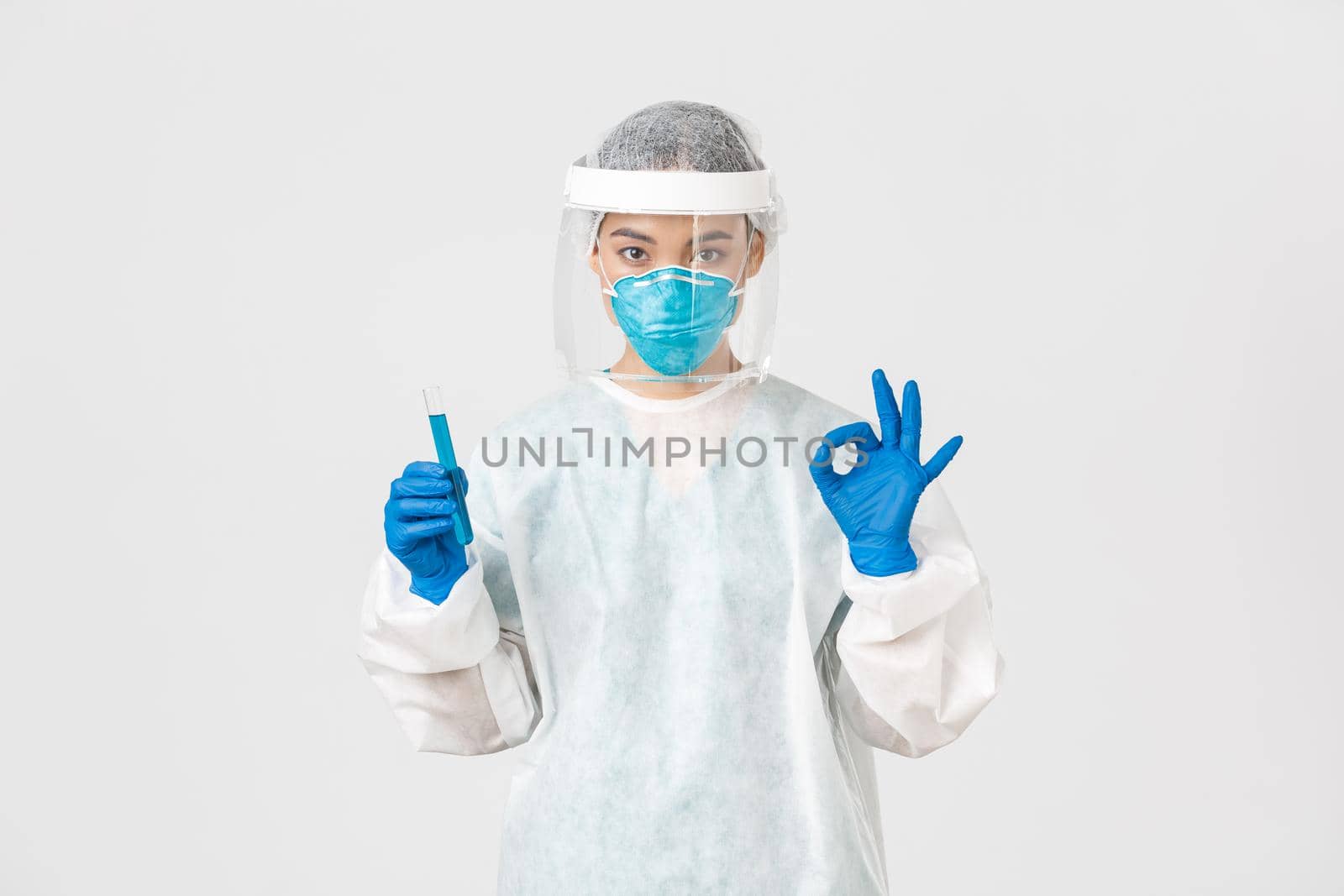 Covid-19, coronavirus disease, healthcare workers concept. Serious asian female doctor, professional researcher in personal protective equipment showing okay gesture, holding test-tube with vaccine.