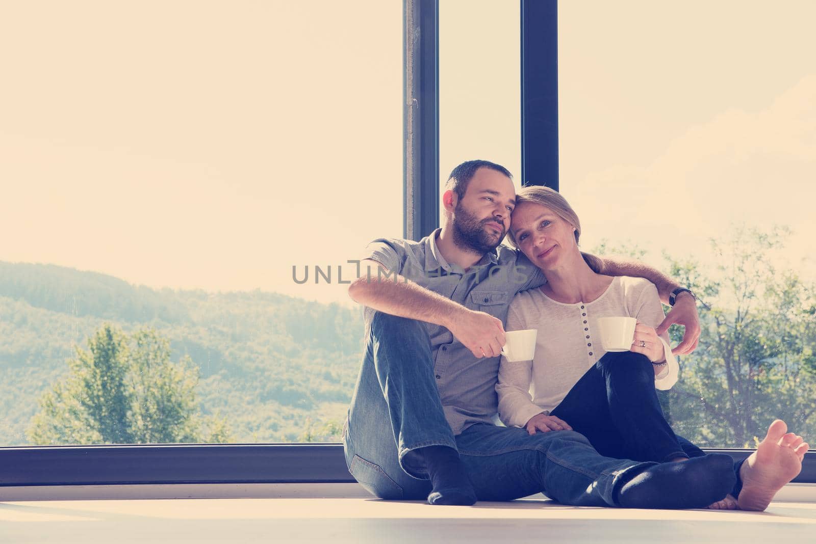 happy romantic couple enjoying morning coffee on the floor by the window in their luxury home