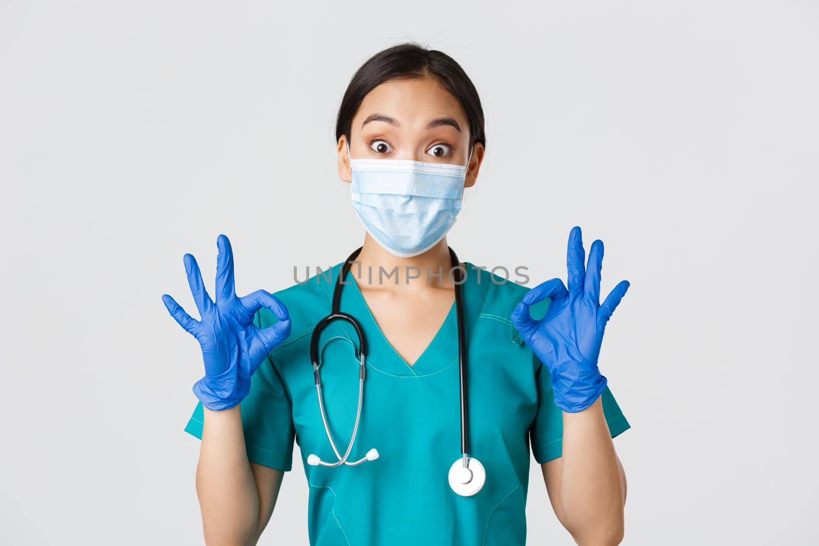 Covid-19, coronavirus disease, healthcare workers concept. Excited and impressed asian doctor, nurse in medical mask and rubber gloves showing okay gesture, approve or praise nice work by Benzoix