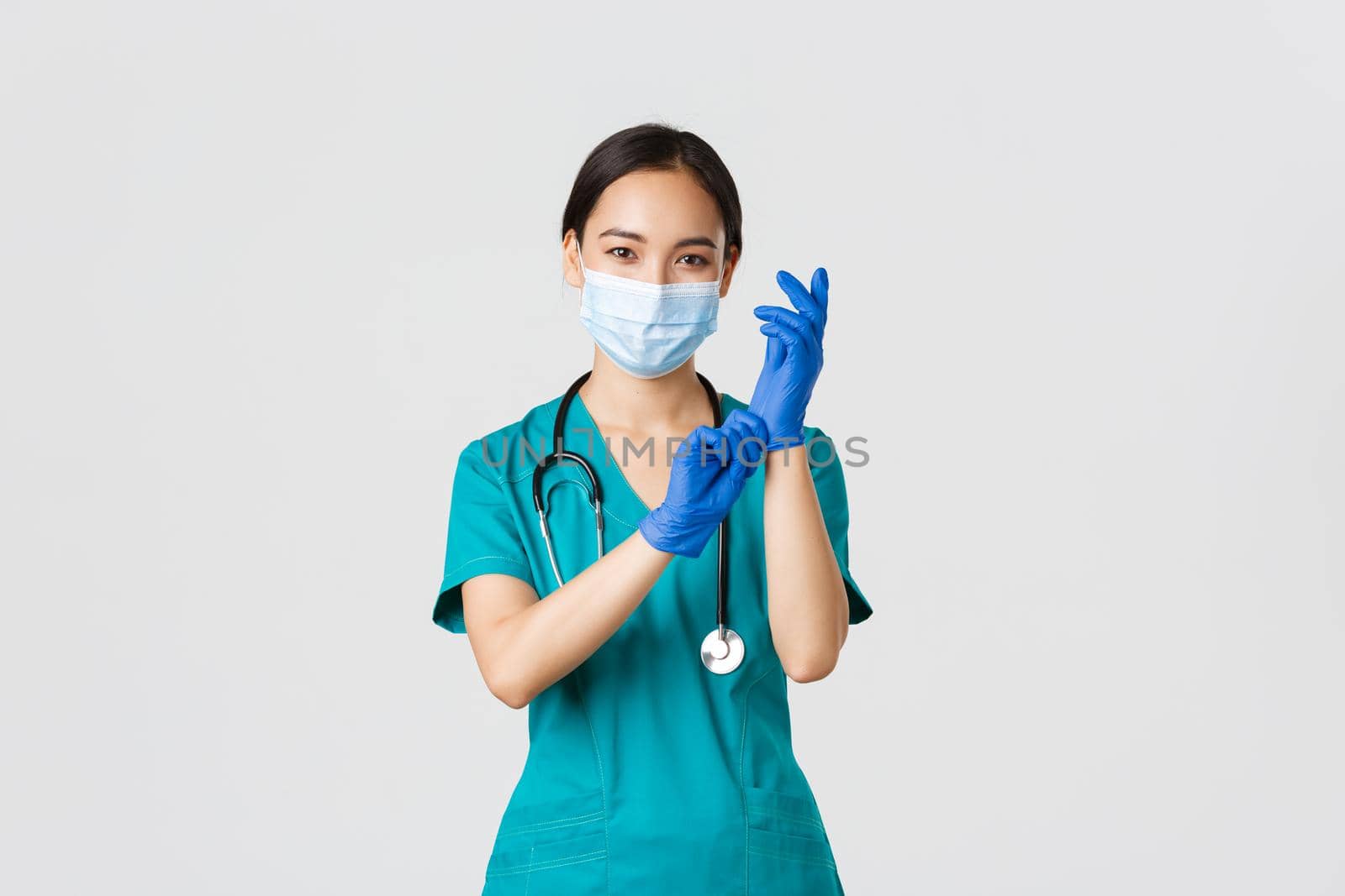 Covid-19, coronavirus disease, healthcare workers concept. Professional and confident smiling asian physician, nurse wear rubber gloves and medical mask for patient examination, white background.