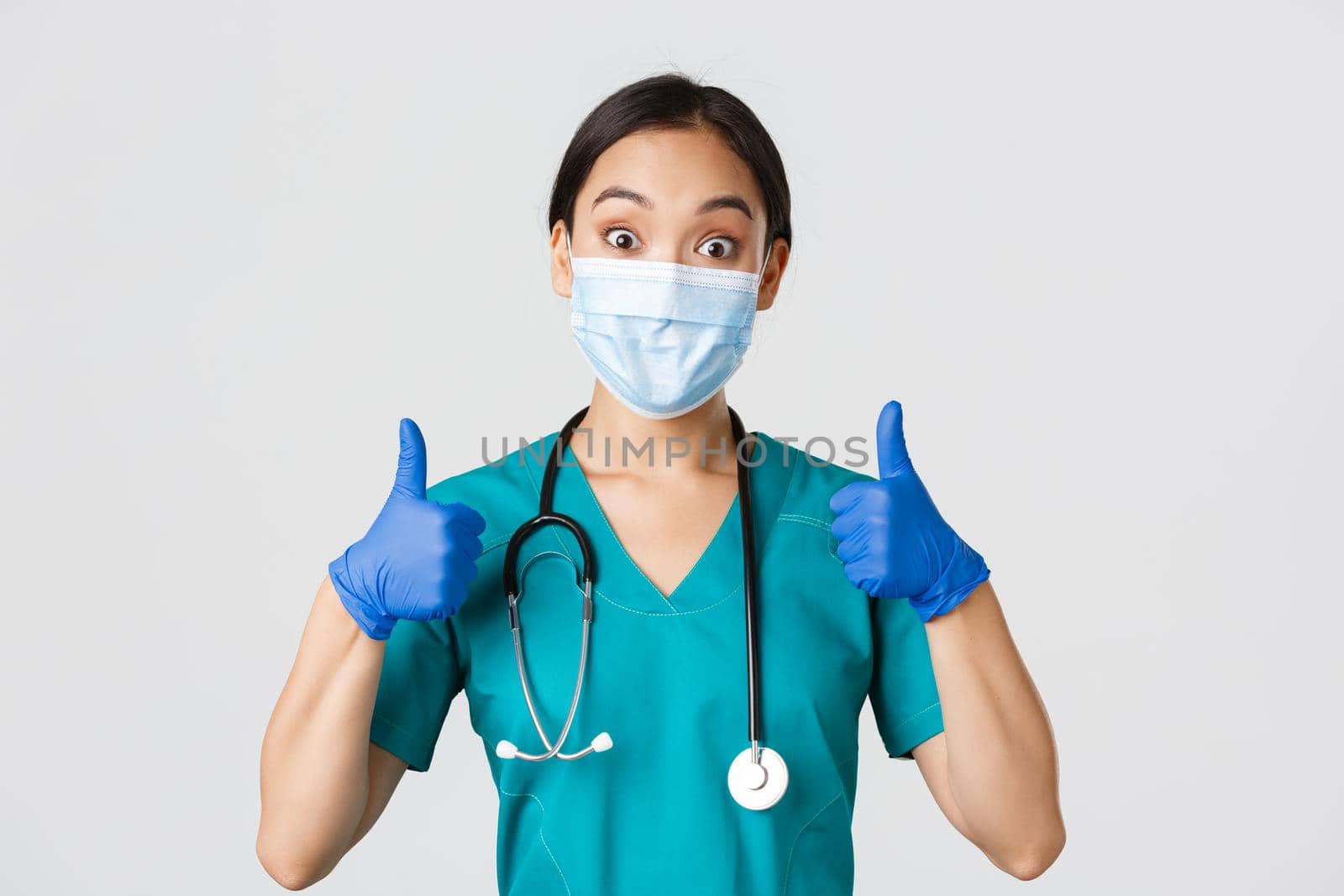 Covid-19, coronavirus disease, healthcare workers concept. Amused smiling asian doctor, physician in medical mask and rubber gloves, showing thumbs-up, approve, praise nice work by Benzoix
