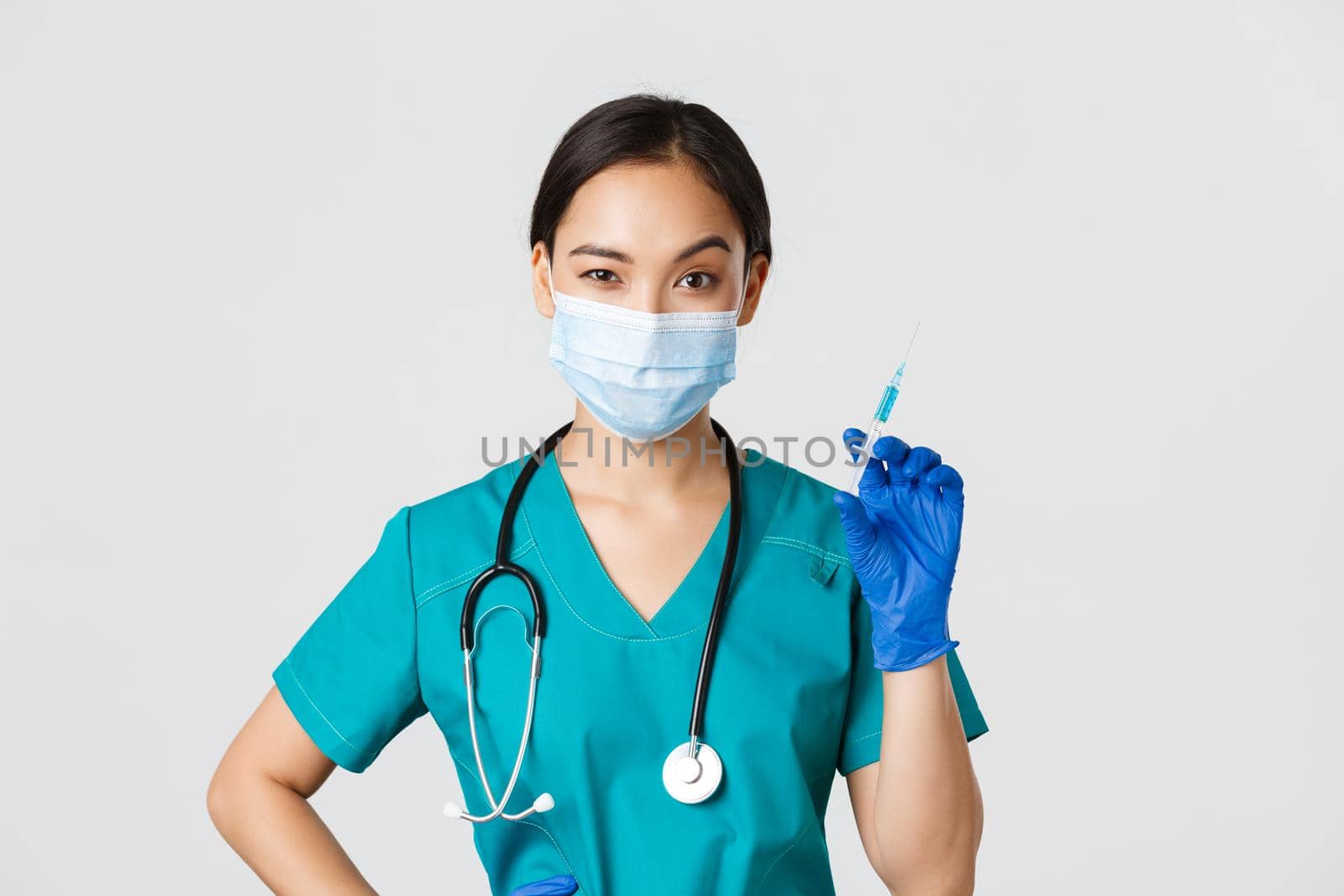 Covid-19, coronavirus disease, healthcare workers concept. Sassy cute asian female nurse, intern in medical mask and gloves holding syringe with vaccine, ready to make shot, white background.