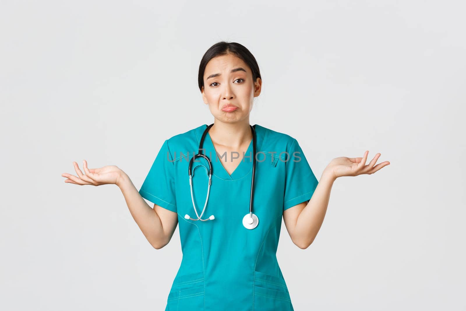 Covid-19, healthcare workers, pandemic concept. Portrait of clueless asian female nurse, woman doctor shrugging and spread hands sideways unaware, dont know, cant help, white background.