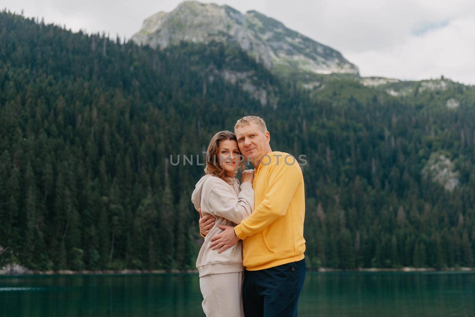 Romantic wedding couple in love standing on the stony shore of the lake, Scenic mountain view. The bride and groom. Beautiful caucasian couple hugging by the lake at summer sunny day. Honeymoon concept.
