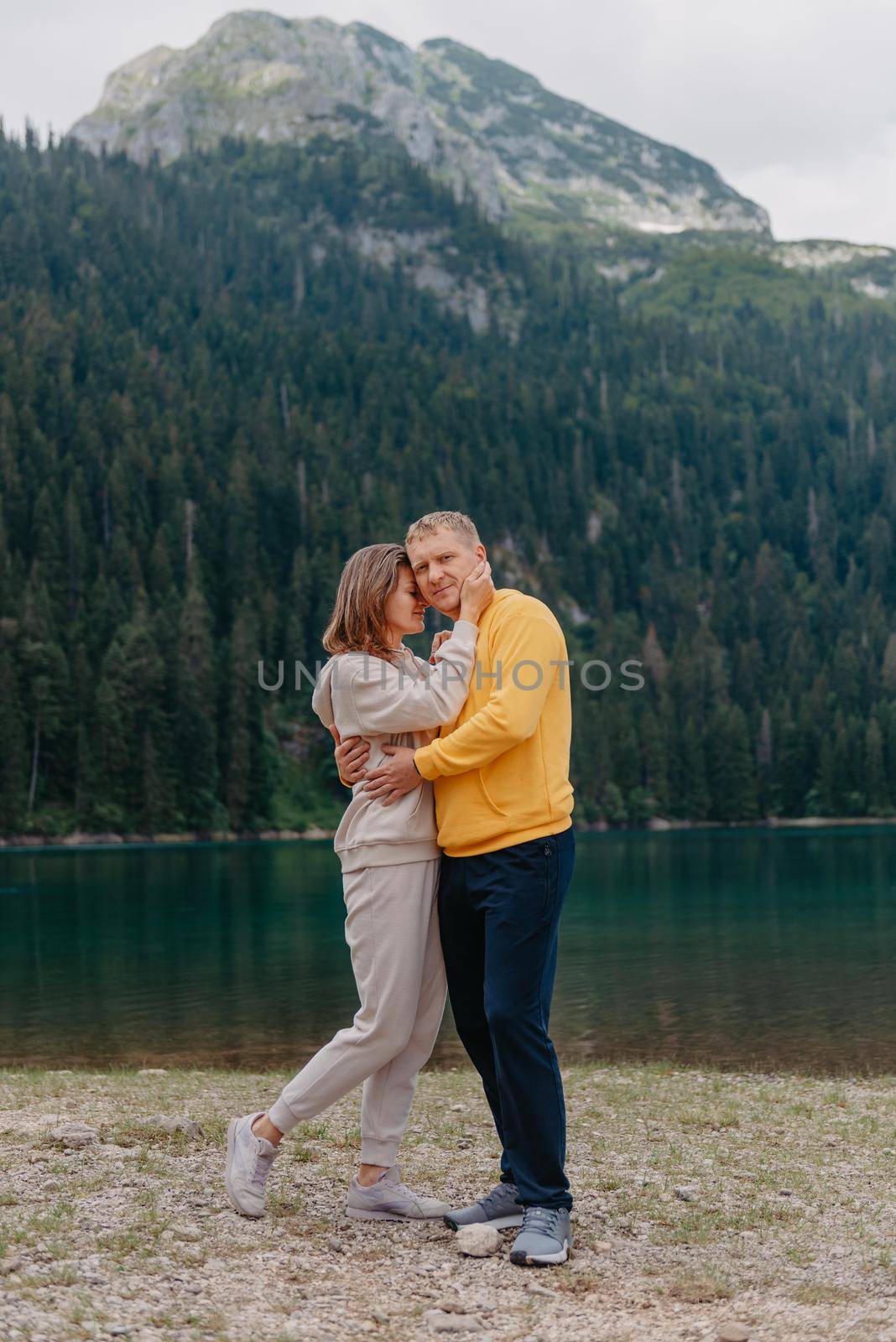 Romantic wedding couple in love standing on the stony shore of the lake, Scenic mountain view. The bride and groom. Beautiful caucasian couple hugging by the lake at summer sunny day. Honeymoon concept.