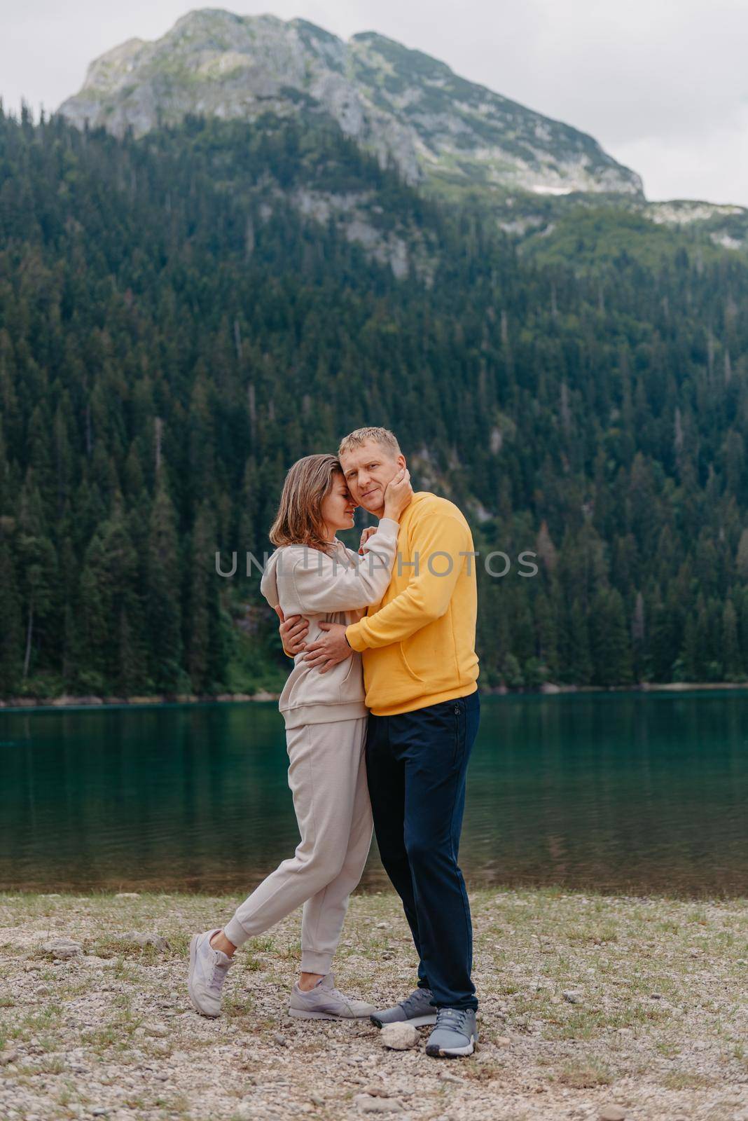 Romantic wedding couple in love standing on the stony shore of the lake, Scenic mountain view. The bride and groom. Beautiful caucasian couple hugging by the lake at summer sunny day. Honeymoon concept. by Andrii_Ko