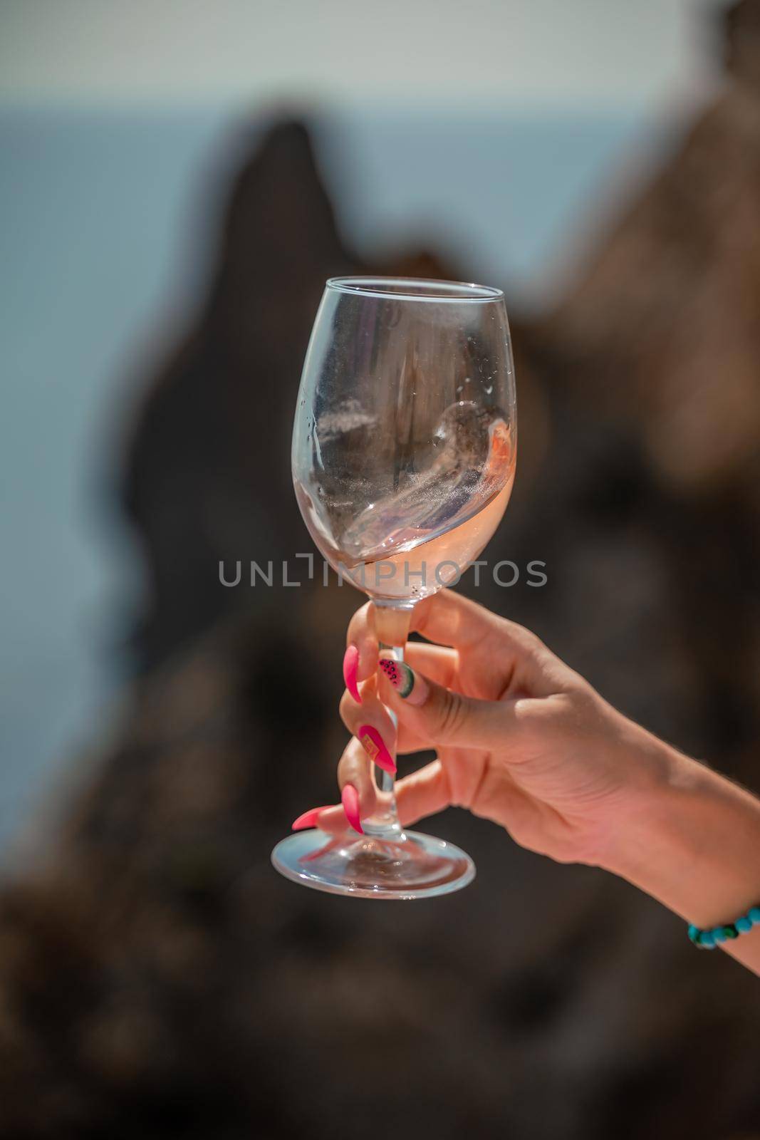 A female hand holds a glass of wine against the background of the sea and mountains