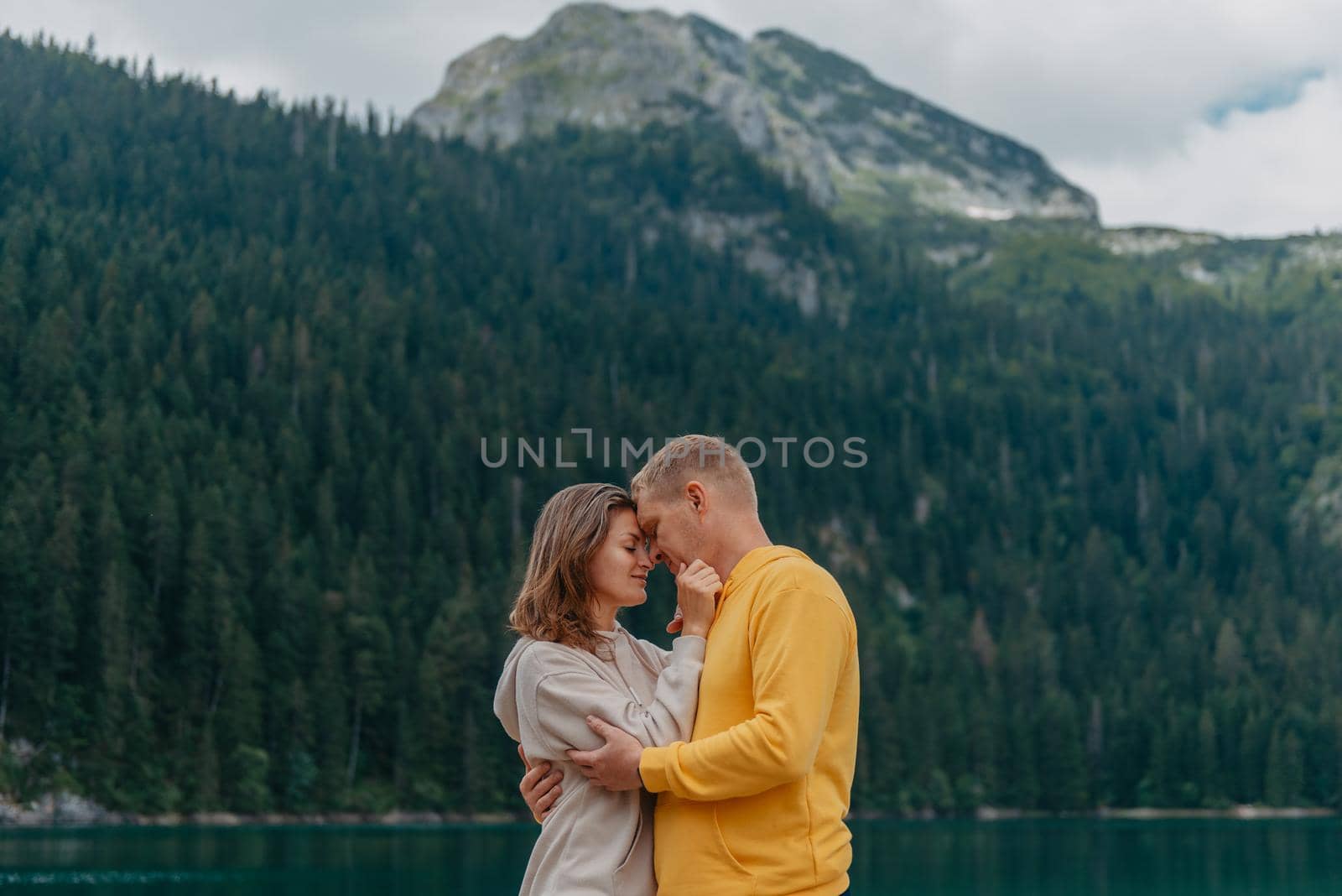 Romantic wedding couple in love standing on the stony shore of the lake, Scenic mountain view. The bride and groom. Beautiful caucasian couple hugging by the lake at summer sunny day. Honeymoon concept. by Andrii_Ko