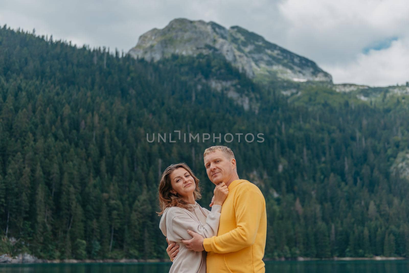 Romantic wedding couple in love standing on the stony shore of the lake, Scenic mountain view. The bride and groom. Beautiful caucasian couple hugging by the lake at summer sunny day. Honeymoon concept. by Andrii_Ko