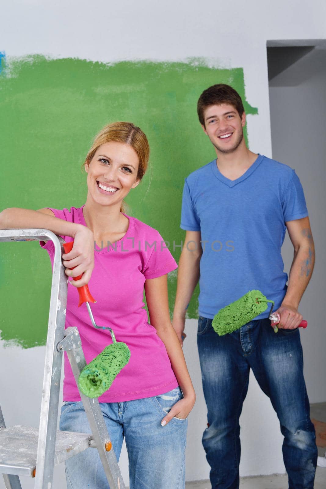 happy young couple paint in green and blue color white wall of their new home