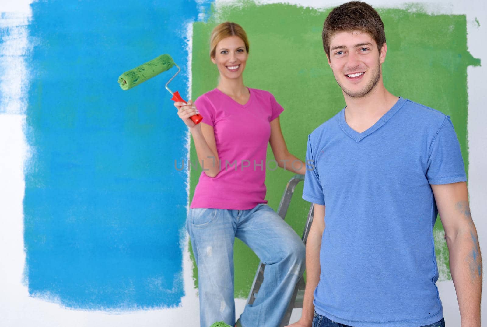 happy young couple paint in green and blue color white wall of their new home