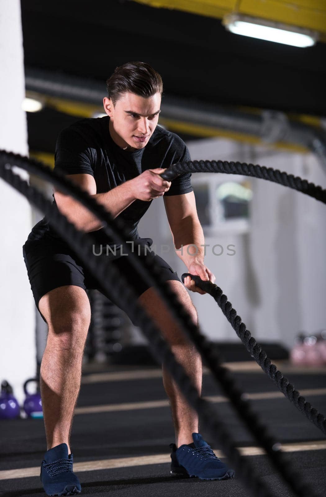 young fit athlete man working out in functional training gym doing  battle ropes exercise as part of cross fitness training