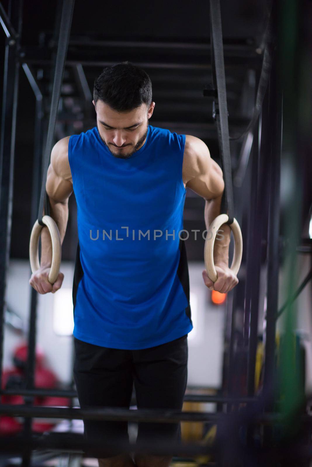 young athlete man working out pull ups with gymnastic rings at the cross fitness gym