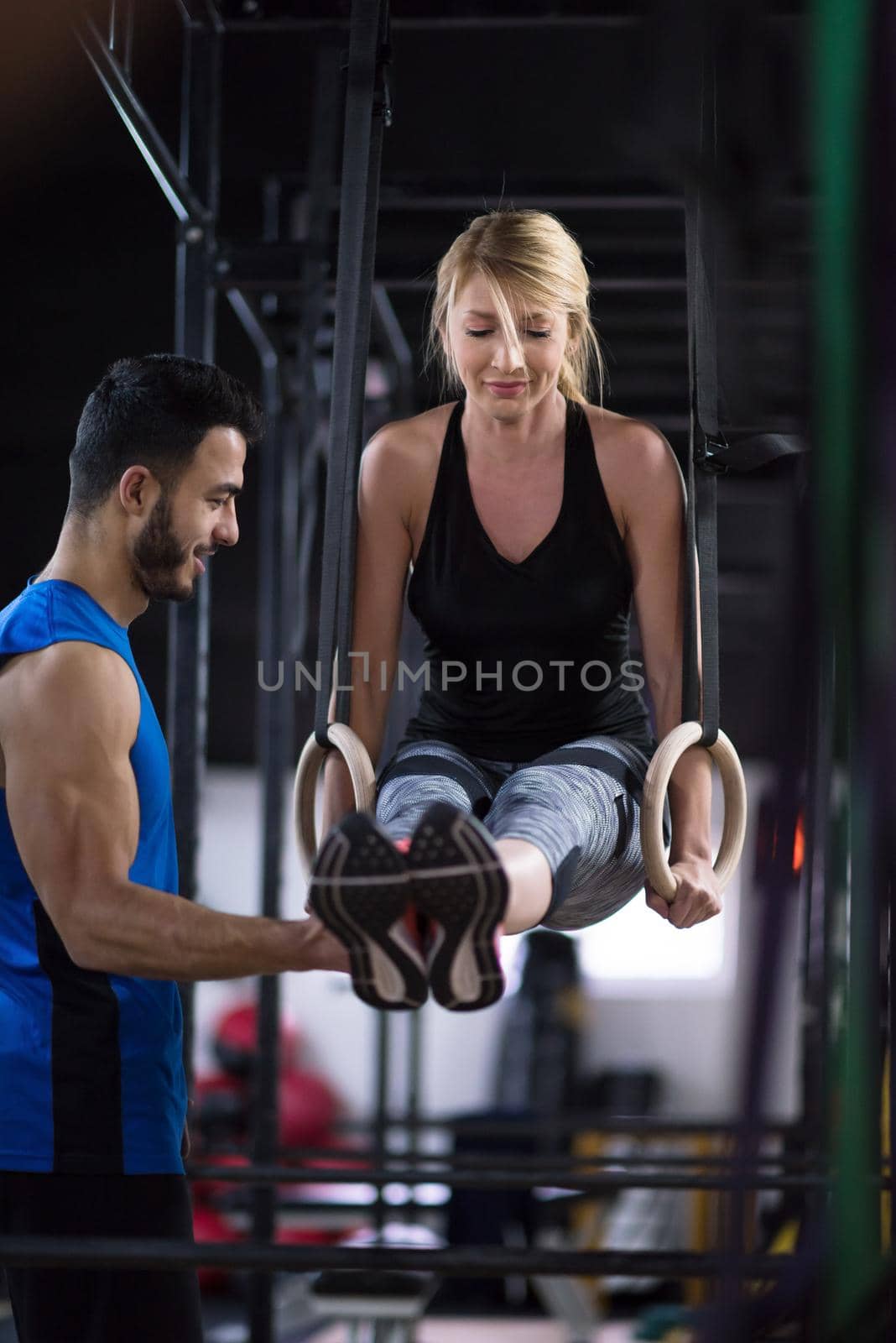 woman working out with personal trainer on gymnastic rings by dotshock