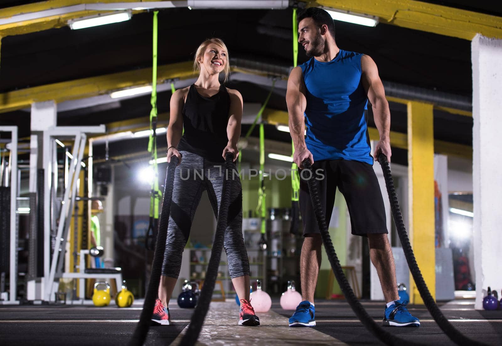 sports couple doing battle ropes cross fitness exercise by dotshock
