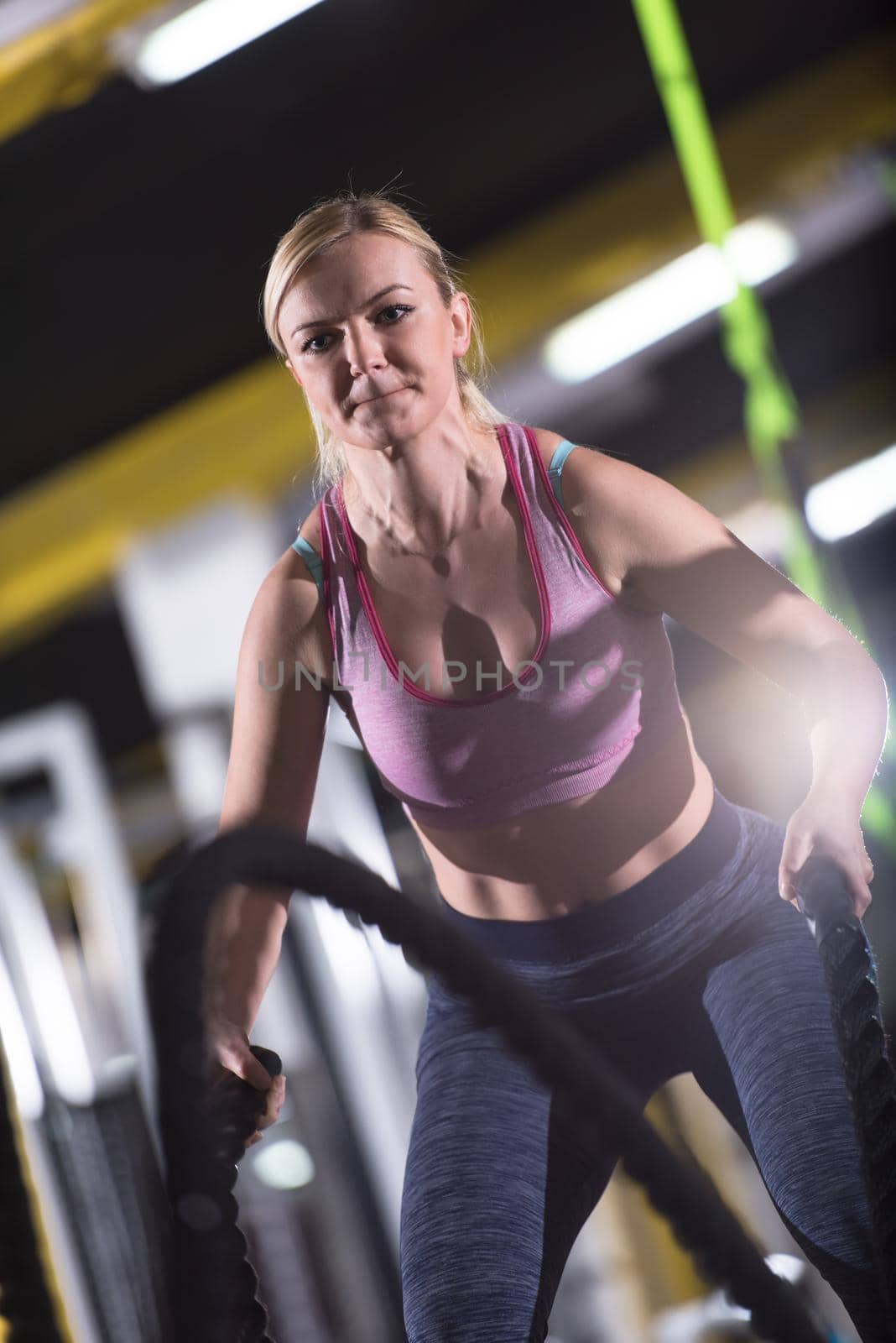 young fit athlete woman working out in functional training gym doing  battle ropes exercise as part of cross fitness training