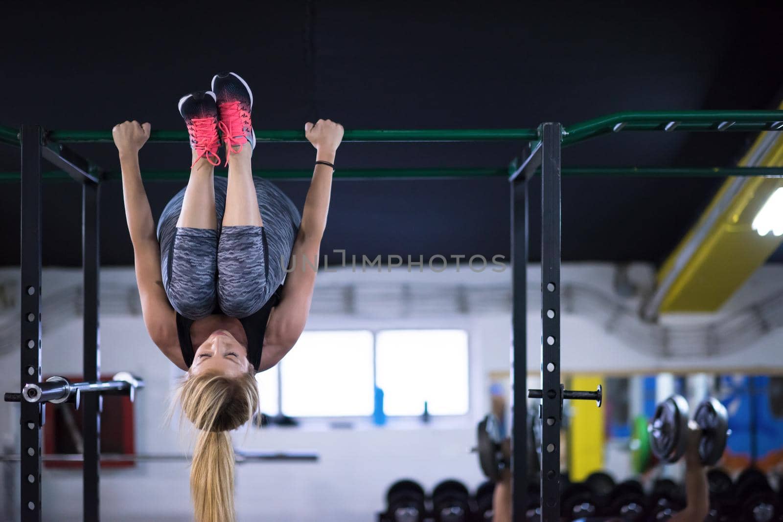 athlete woman doing abs exercises hanging upside down on horizontal bar at cross fitness gym