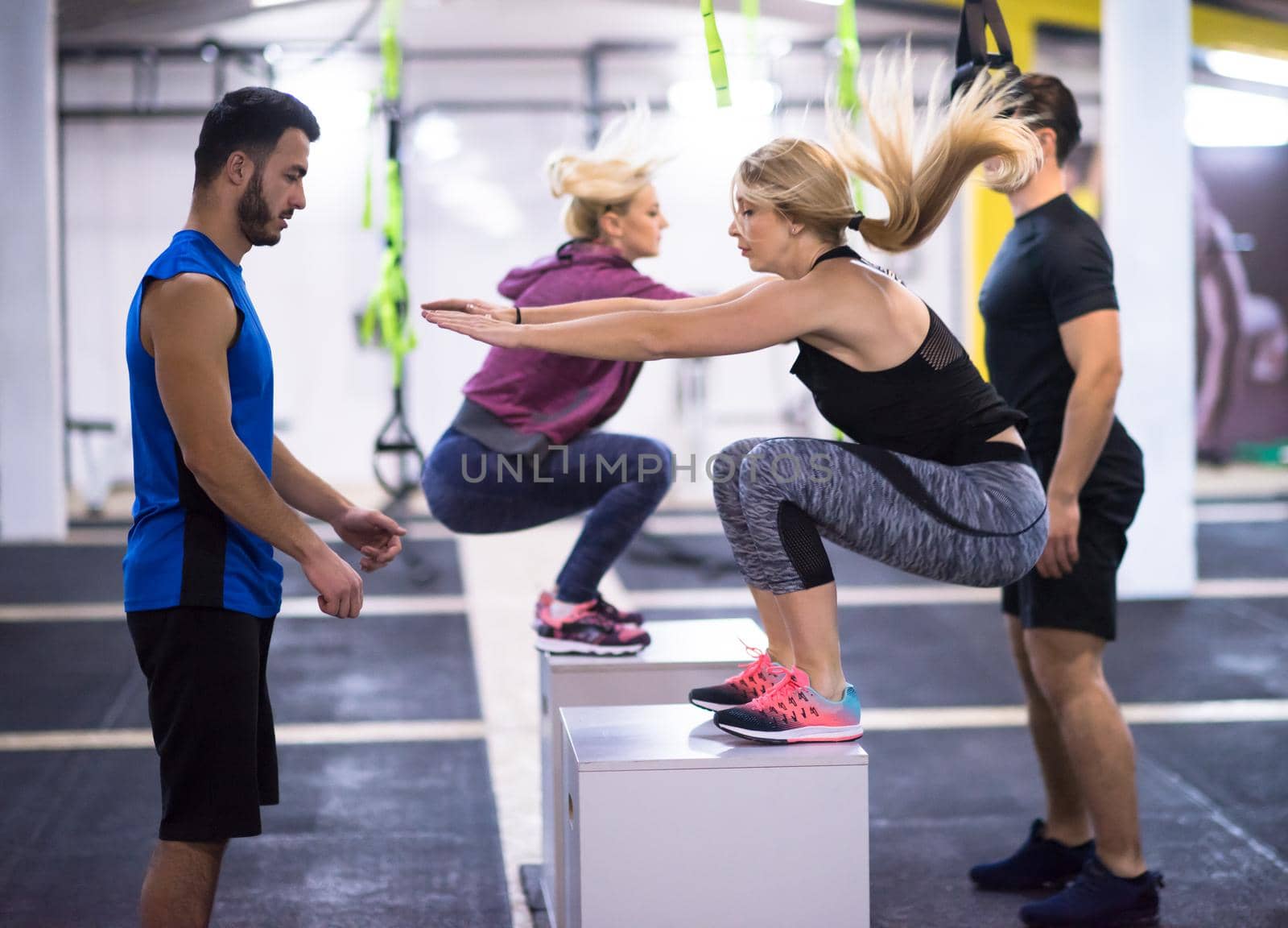 group of young healthy athletic people training jumping on fit box at cross fitness gym