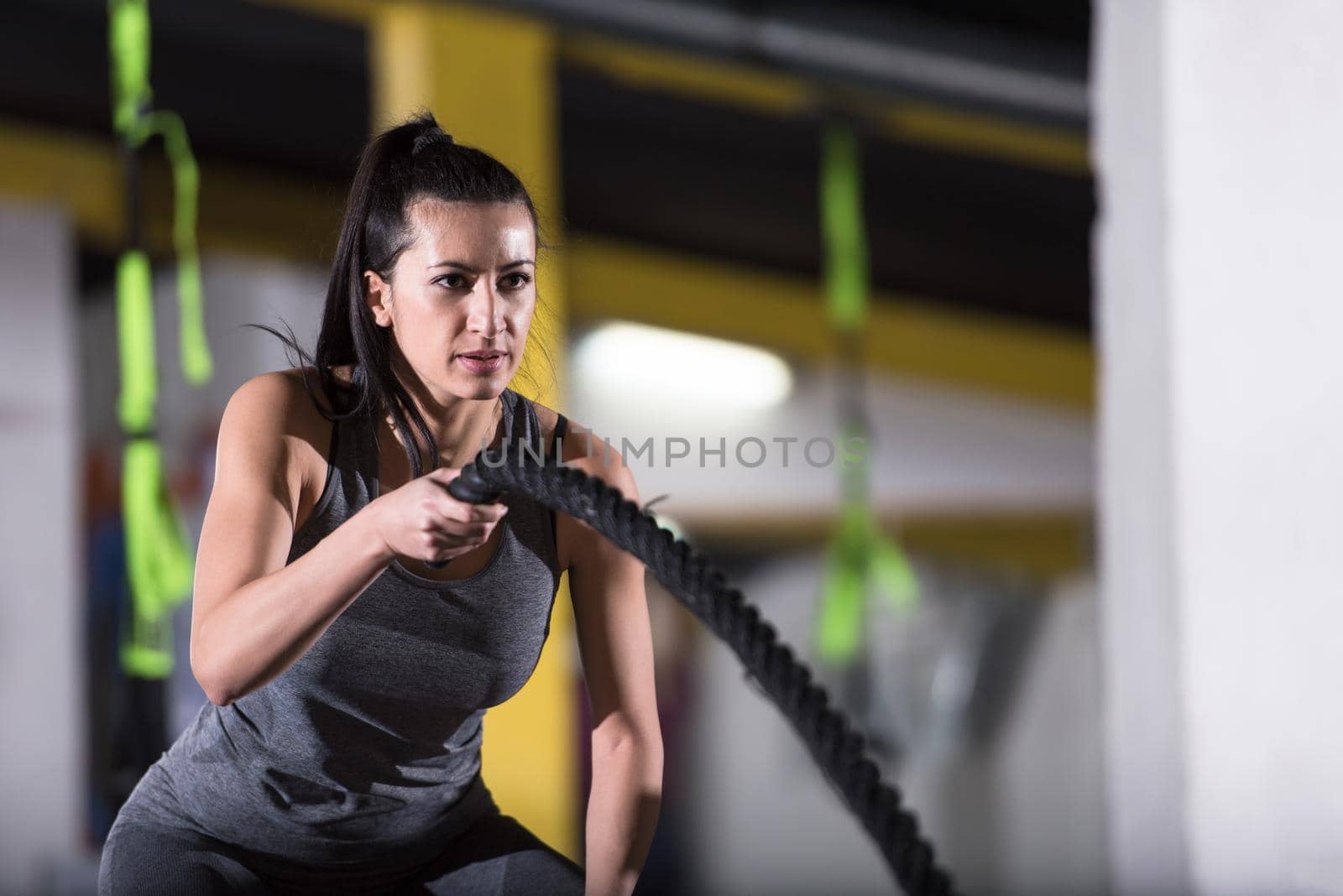 young fit athlete woman working out in functional training gym doing  battle ropes exercise as part of cross fitness training