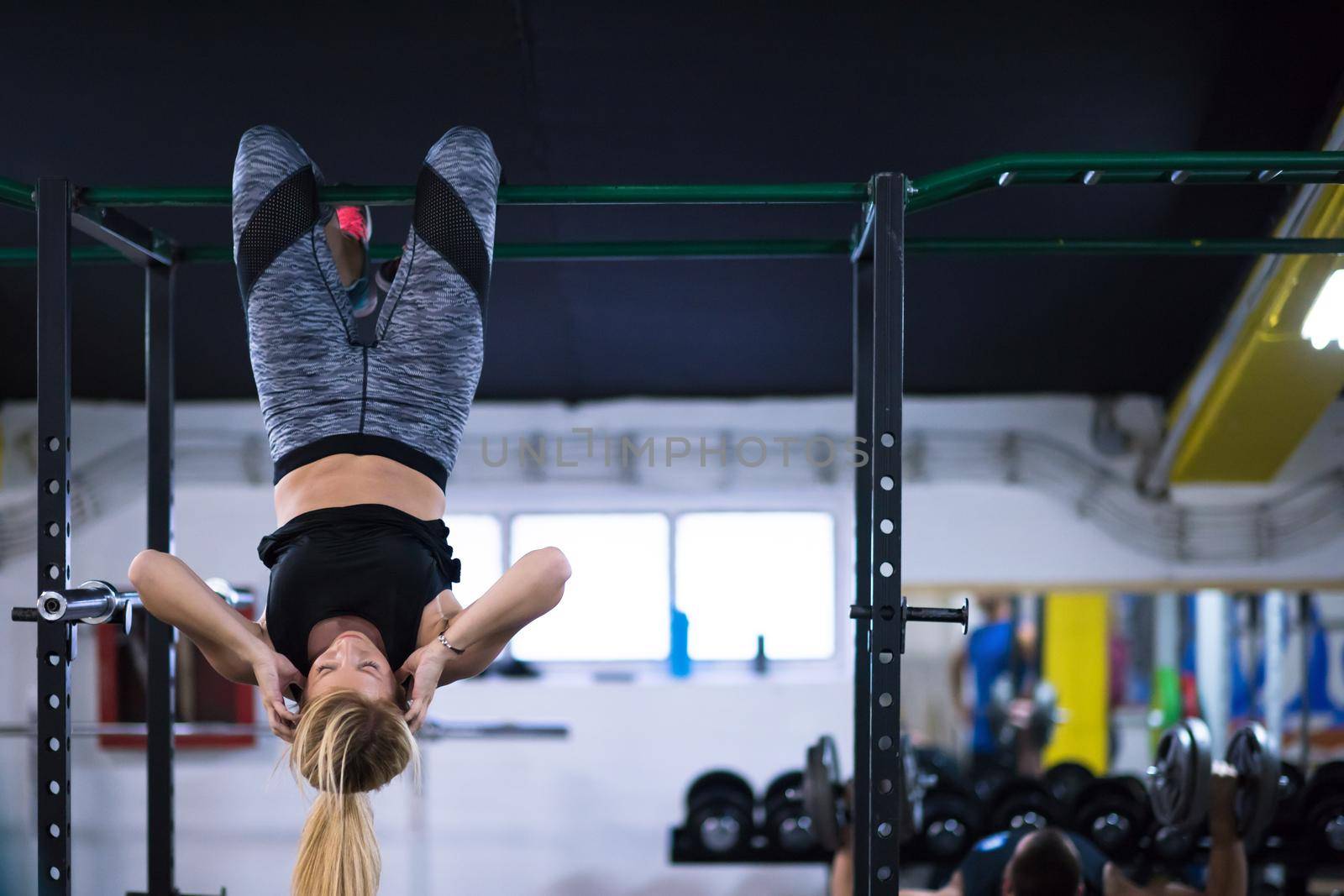 athlete woman doing abs exercises hanging upside down on horizontal bar at cross fitness gym