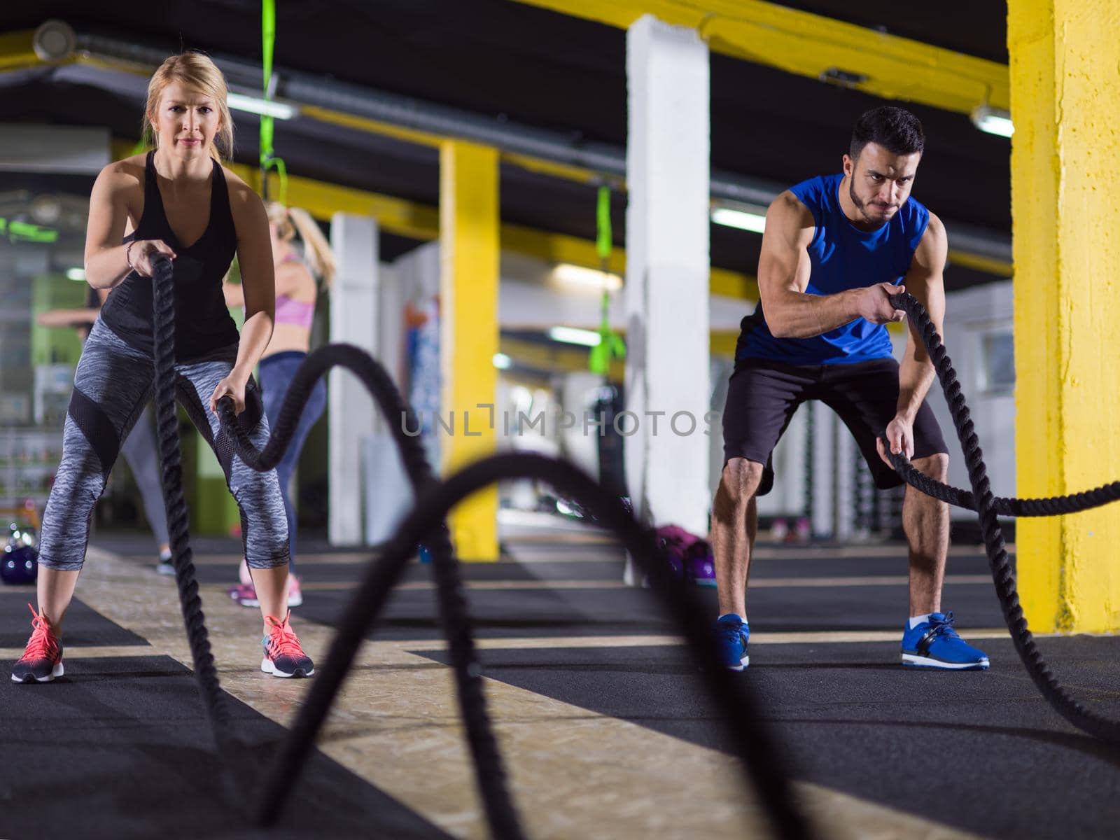 young fit sports couple working out in functional training gym doing fitness exercise with battle ropes