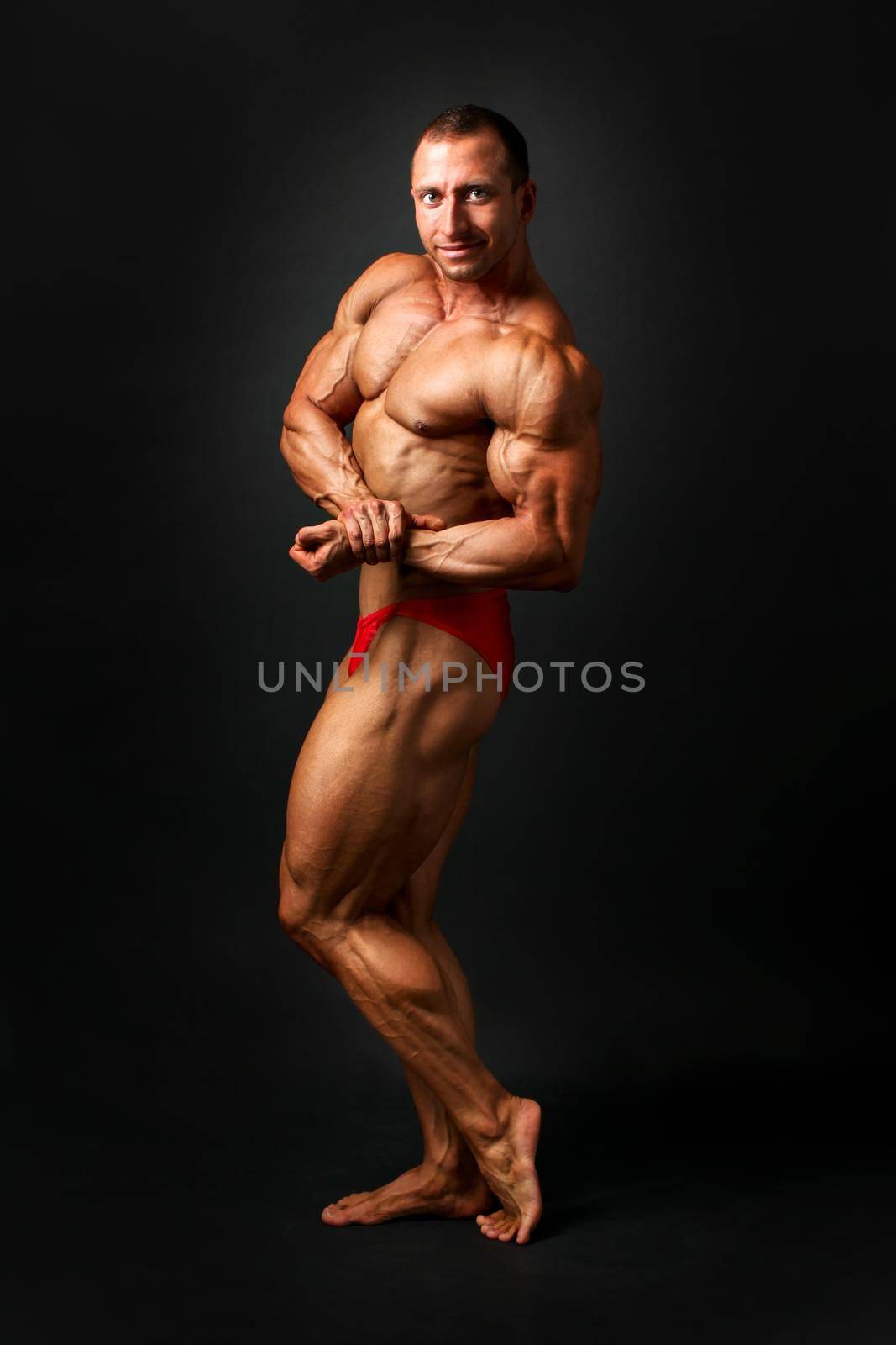 Studio shot of young male bodybuilder posing, showing side biceps and chest pose, on black background. by Ivanko