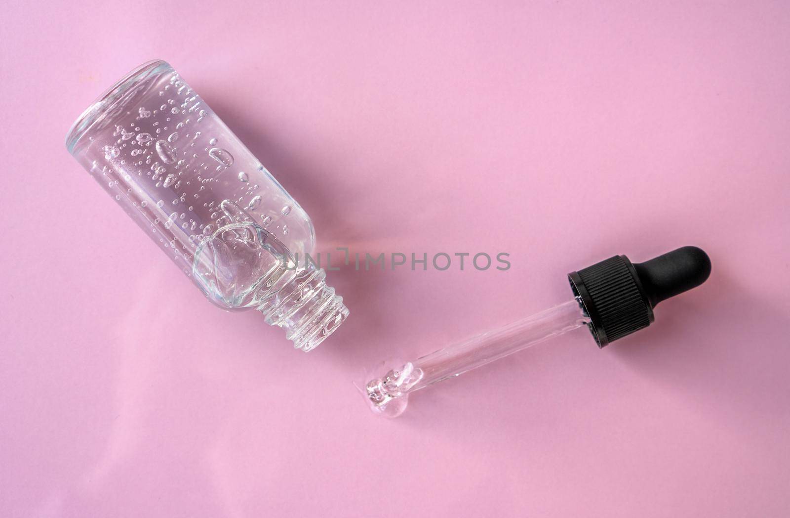 Opened transparent glass dropper bottle with air bubbles on pink background. Pipette with fluid hyaluronic acid, serum, retinol. Cosmetics and healthcare concept Flat lay. Luxury beauty product