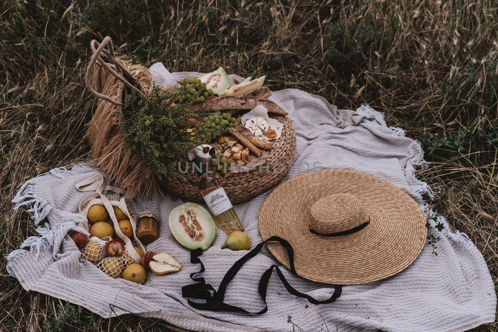 Wine and assorted products for the summer picnic are served on a blanket outdoors by Matiunina