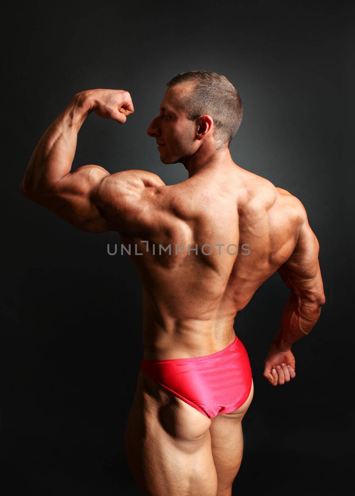 Studio shot of young male bodybuilder posing, showing his biceps and back muscles. by Ivanko