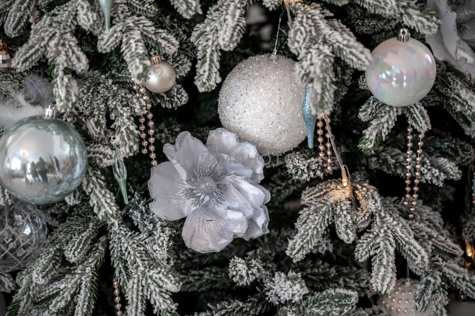 Close-up of a festively decorated outdoor Christmas tree with balls on a blurred sparkling fairy background. Defocused garland lights, bokeh effect