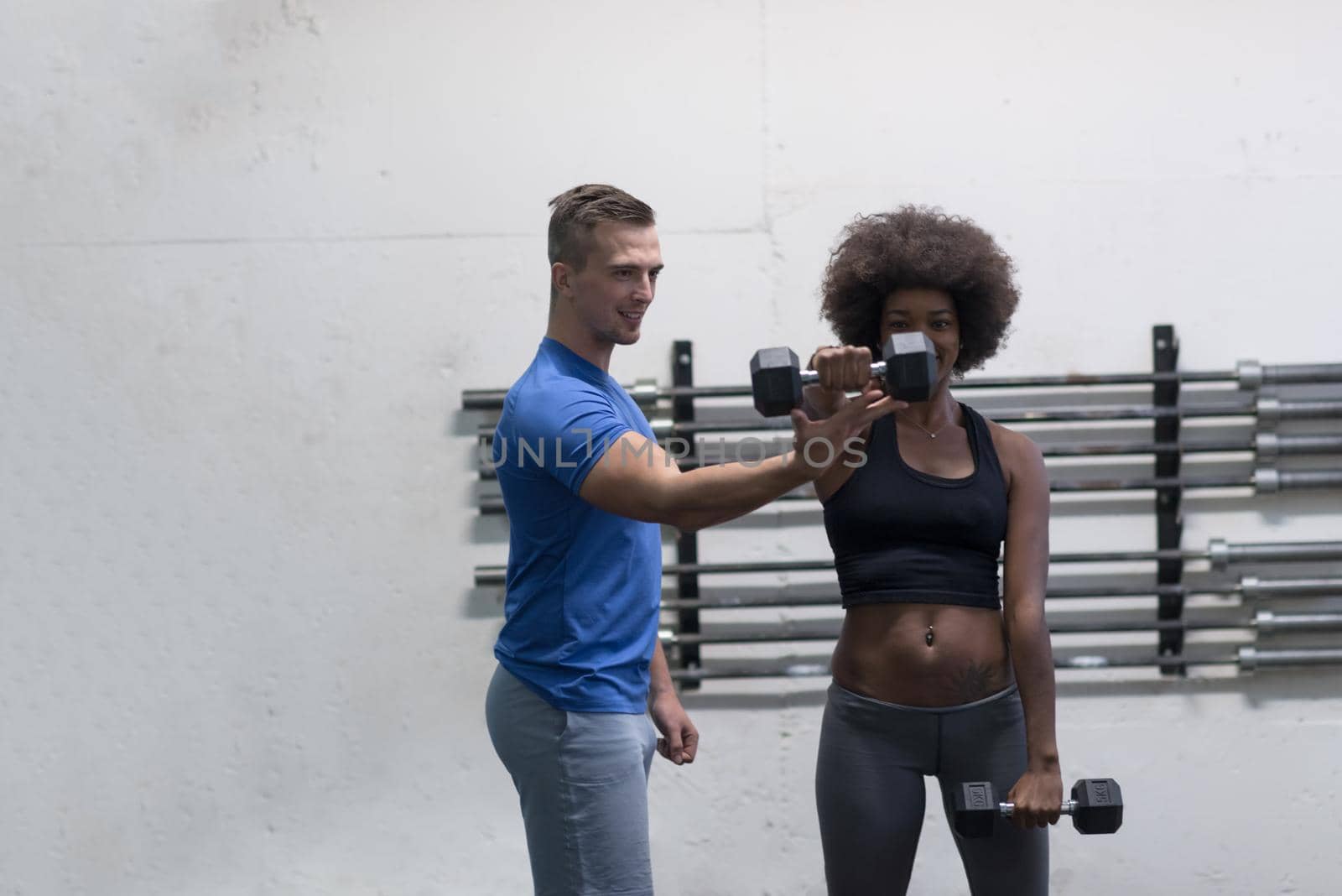 young beautiful African American woman doing bicep curls with fitness trainer in a gym