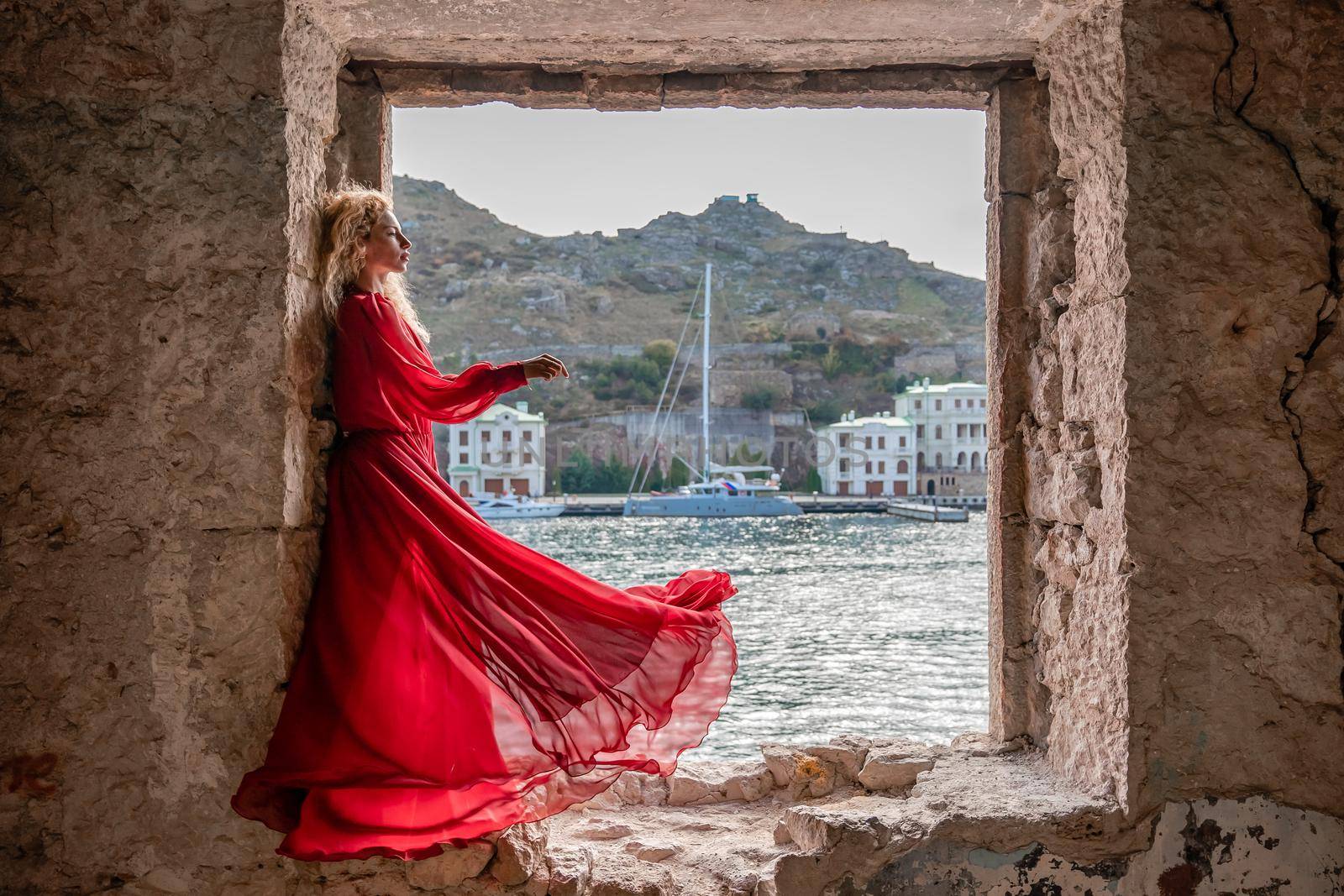 View of Balaklava Bay through an arched balcony in oriental style. The girl in a long red dress stands with her back. Abandoned mansion on the Black Sea coast.