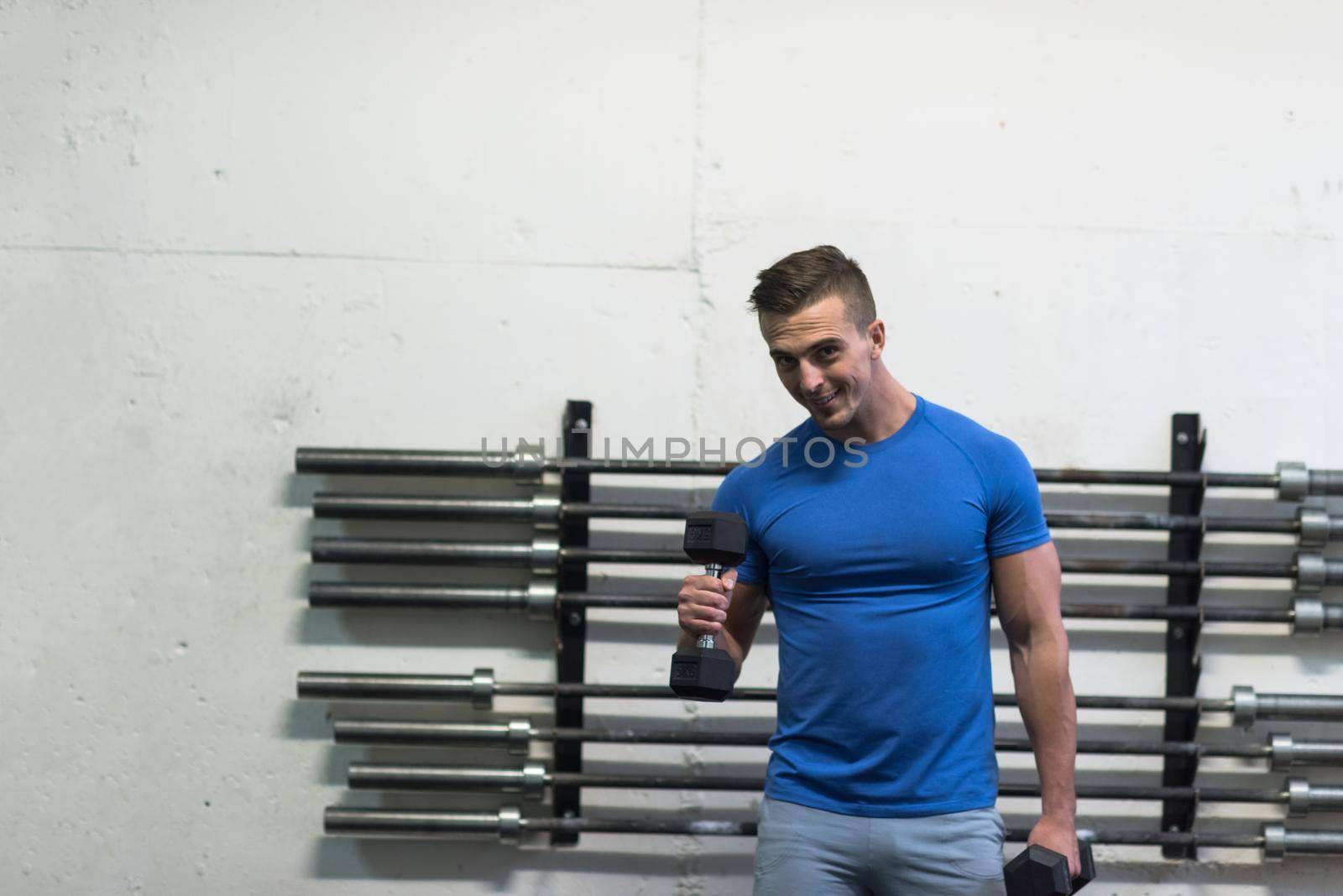 weight training fitness man inside working out arms lifting dumbbells doing biceps curls. Male sports model exercising indoors as part of healthy lifestyle.