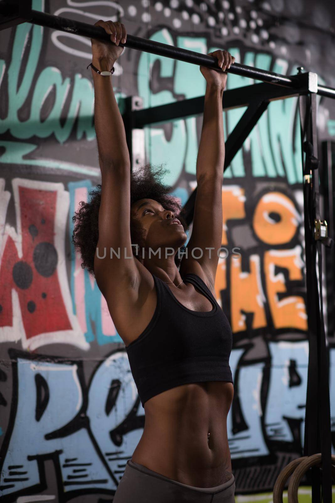 young beautiful african american woman athlete doing pull ups on the horizontal bar in the gym