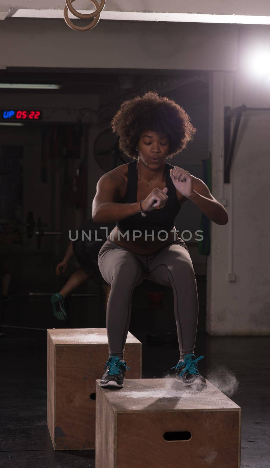 Fit young african american woman box jumping at a crossfit style gym. Female athlete is performing box jumps at gym.