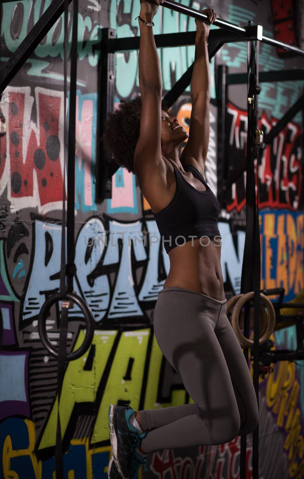 young beautiful african american woman athlete doing pull ups on the horizontal bar in the gym