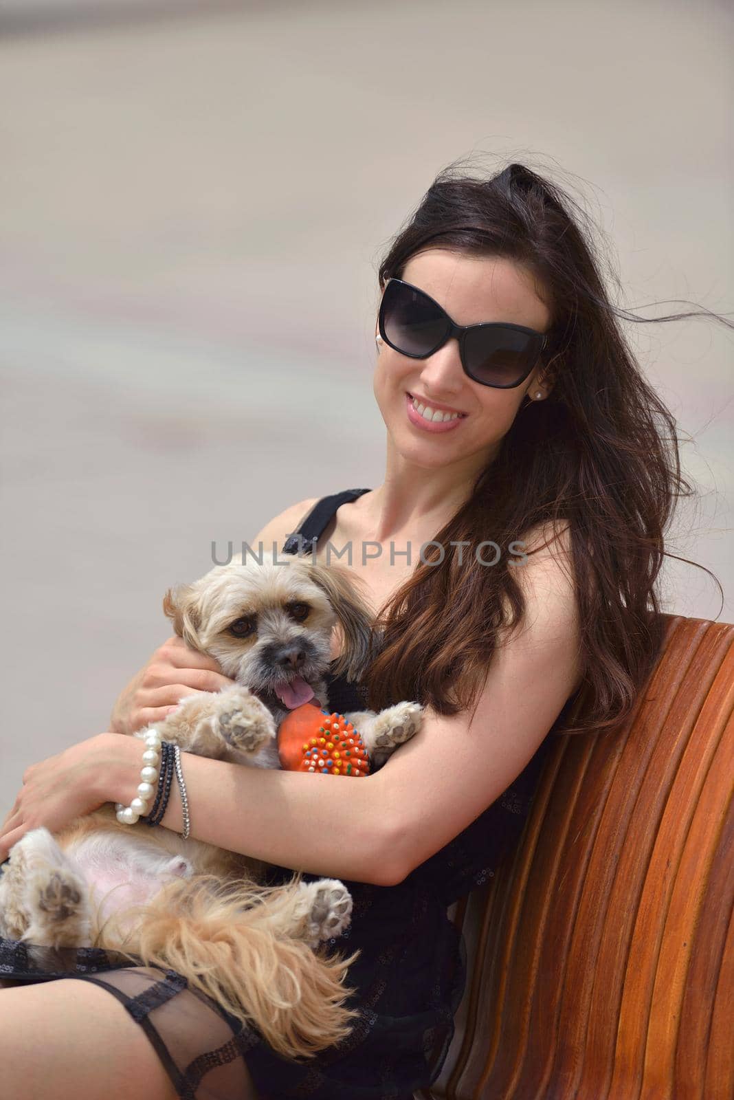 beautiful happy young  woman in black dress with cute small dog puppy have fun on street