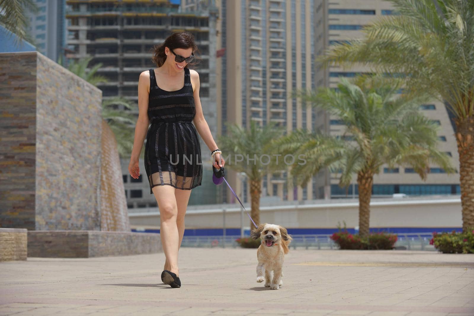 beautiful happy young  woman in black dress with cute small dog puppy have fun on street