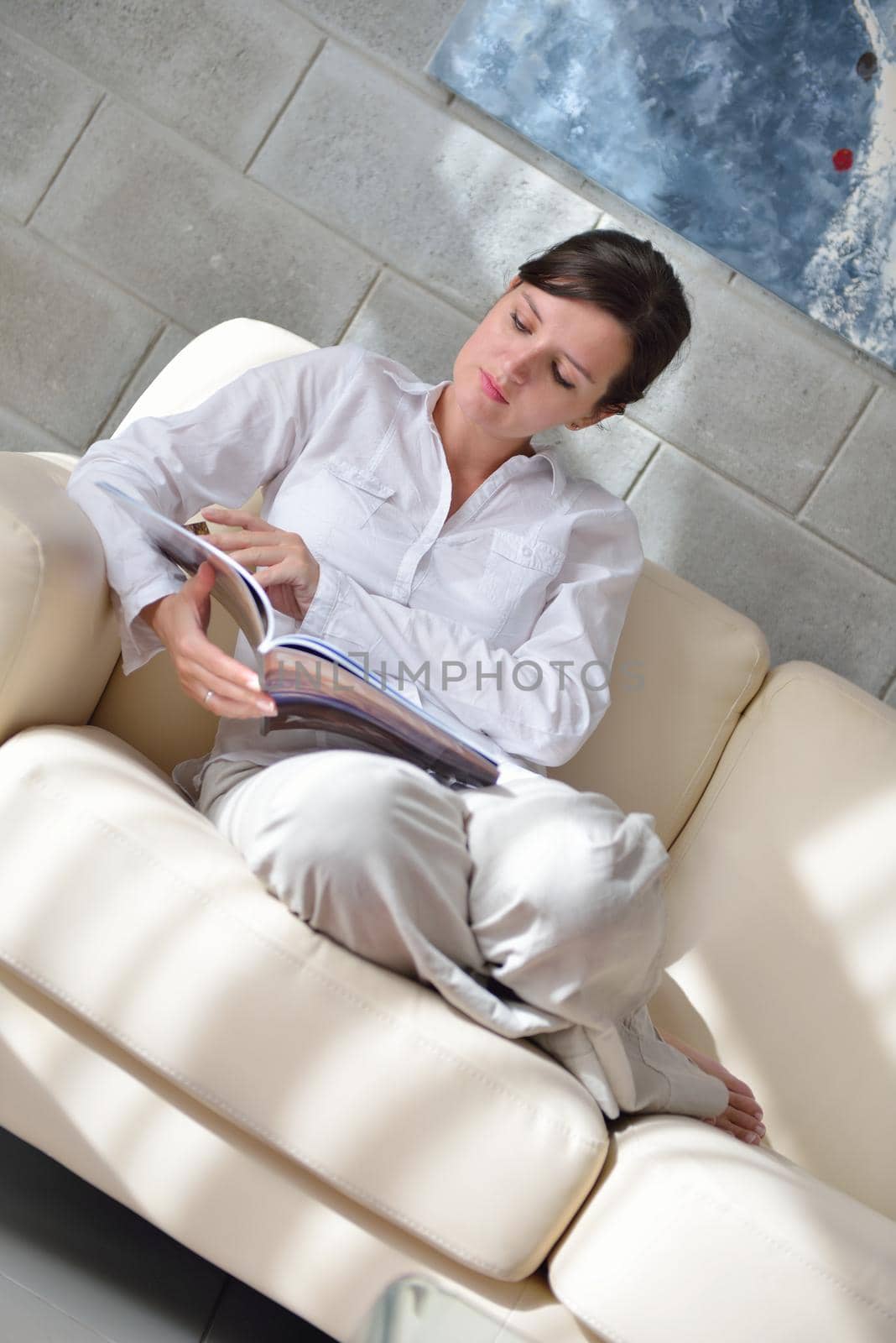 happpy young woman reading magazina at home in comfortabel sofa and bright living room