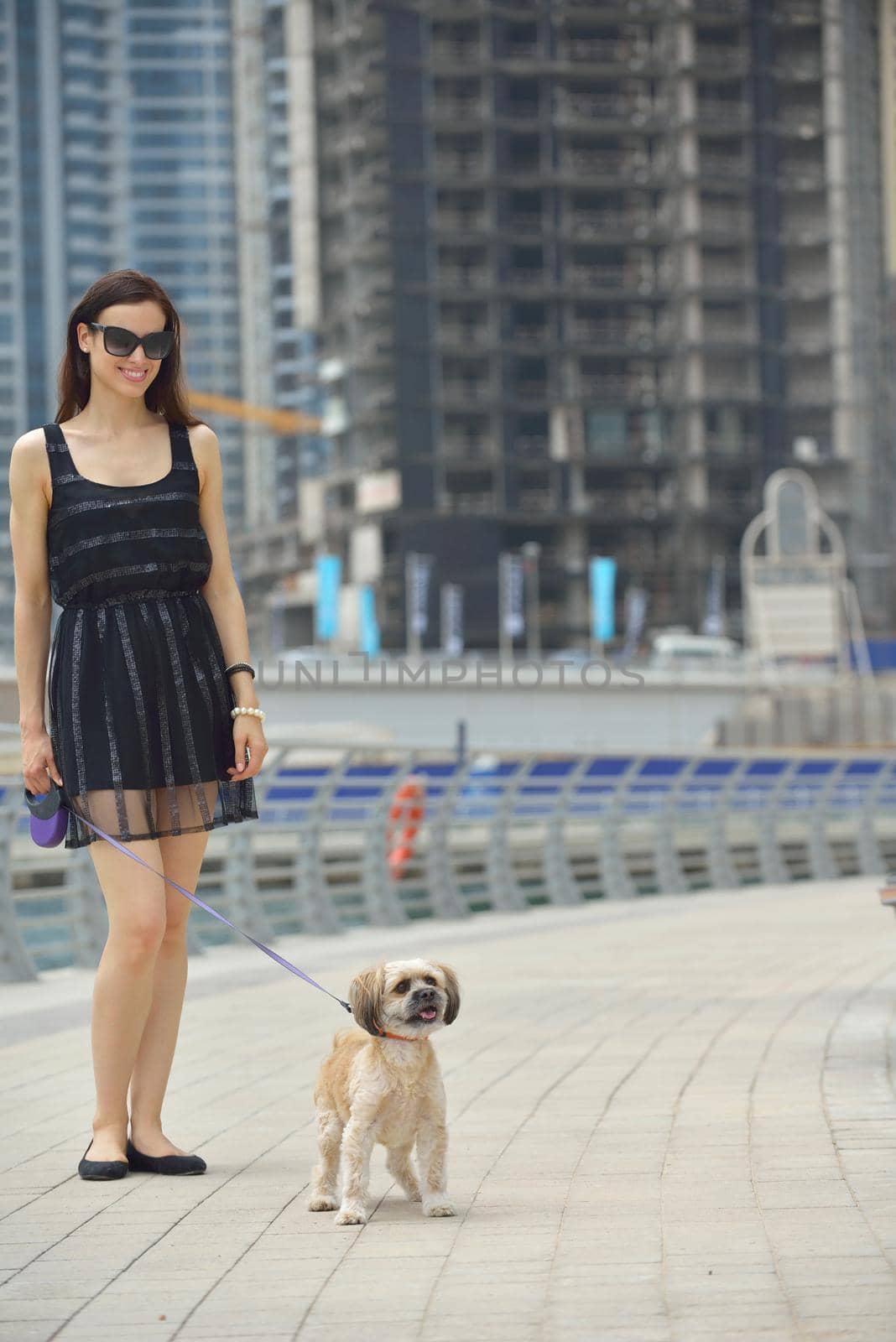 beautiful happy young  woman in black dress with cute small dog puppy have fun on street