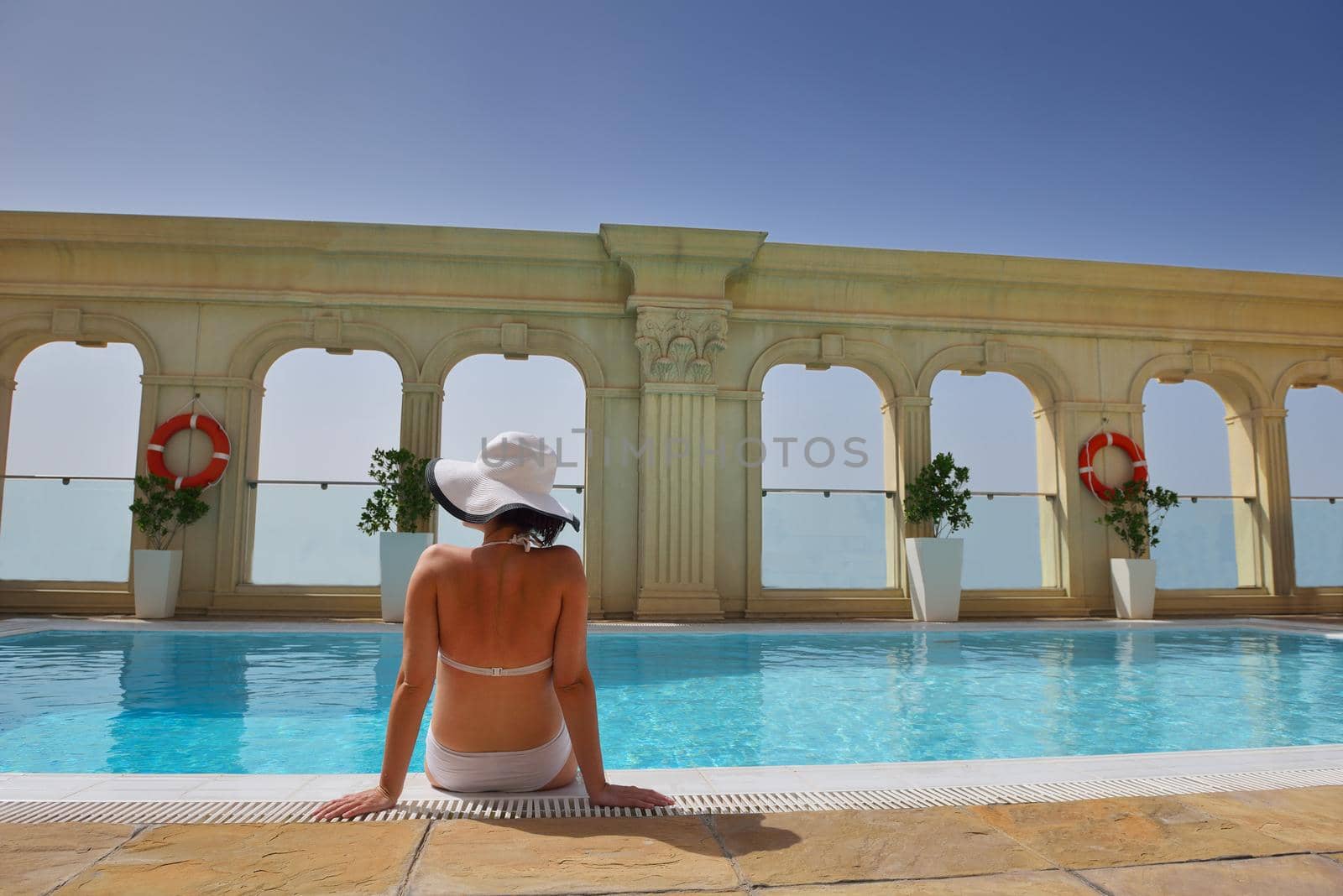 Happy smiling woman with hat and sunglasses  in swimming pool at tropical resort