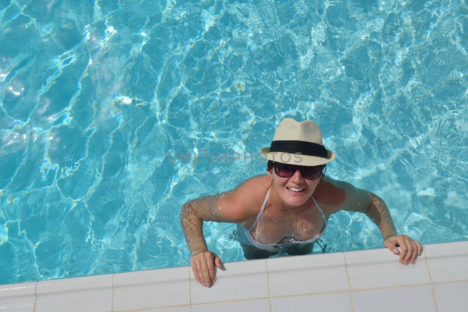 Happy smiling woman with hat and sunglasses  in swimming pool at tropical resort