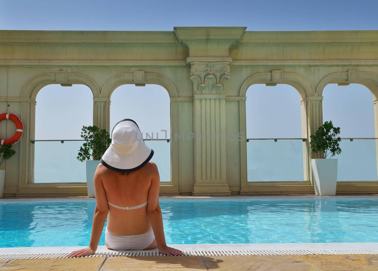 Happy smiling woman with hat and sunglasses  in swimming pool at tropical resort